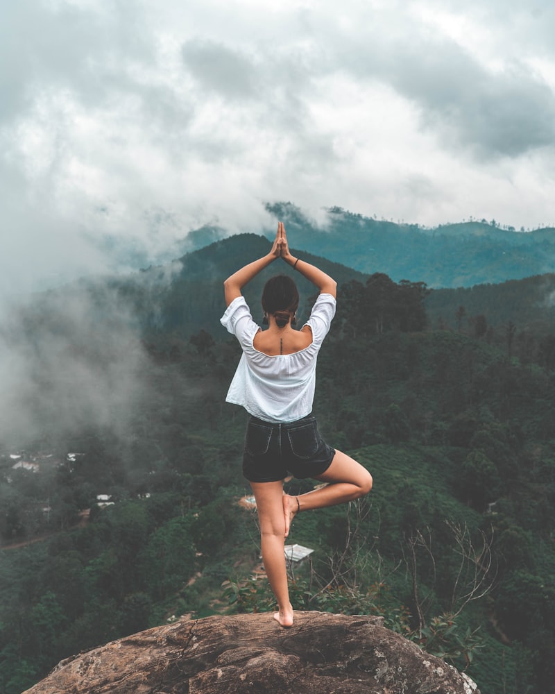 Woman in tree pose standing on a rock overlooking a misty green mountain valley